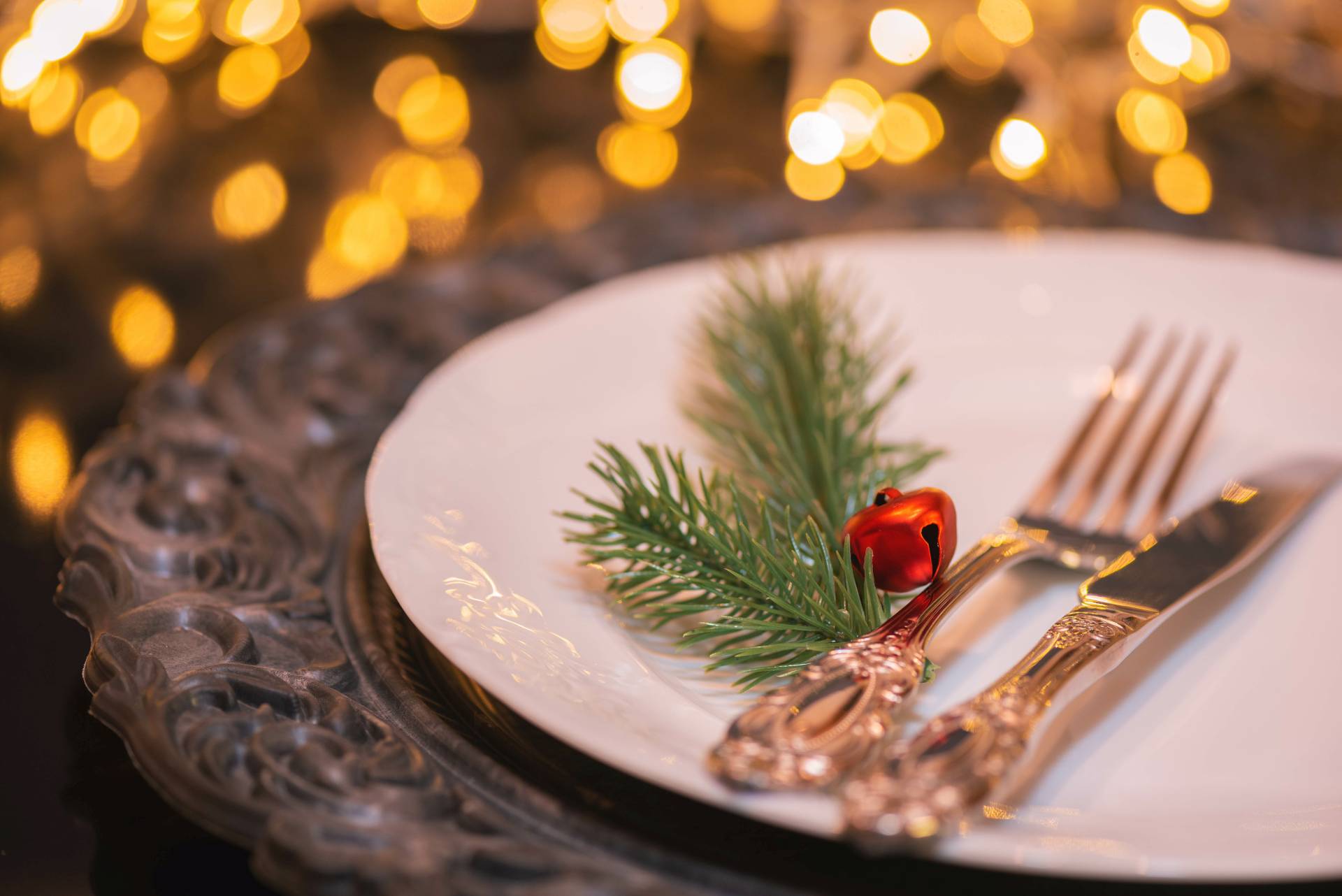 Ein weißer Porzellanteller mit einer verzierten Gabel und einem verzierten Messer mit etwas Weihnachtsdeko und warmen Lichtern im Hintergrund